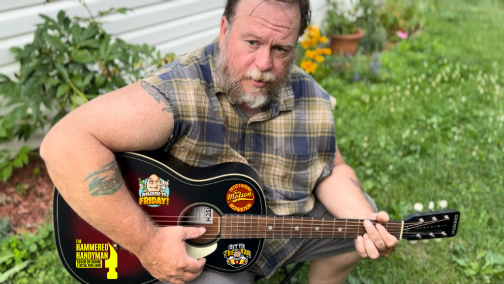 Dan Molson Homepage Header Image. Dan is sitting in the yard playing guitar.